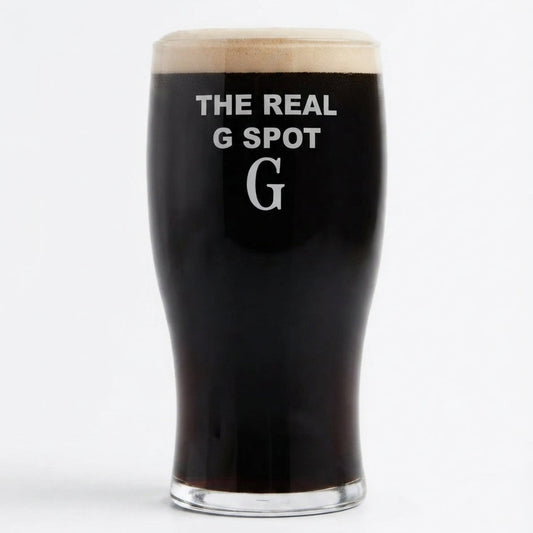 A pint glass filled with black stout beer, featuring the white printed text 'THE REAL G SPOT' and a large letter 'G' on the front, topped with a thick head of foam, set against a plain white background.