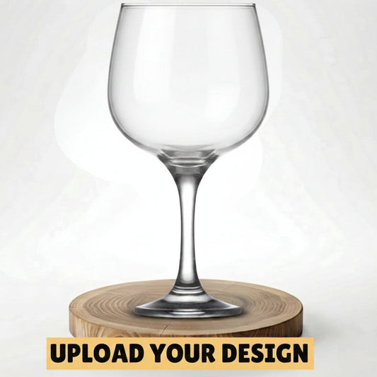 A clear stemmed wine glass with a silver Celtic knot design near the rim, displayed on a round wooden coaster against a light gray background. A yellow banner at the bottom reads 'UPLOAD YOUR DESIGN'.