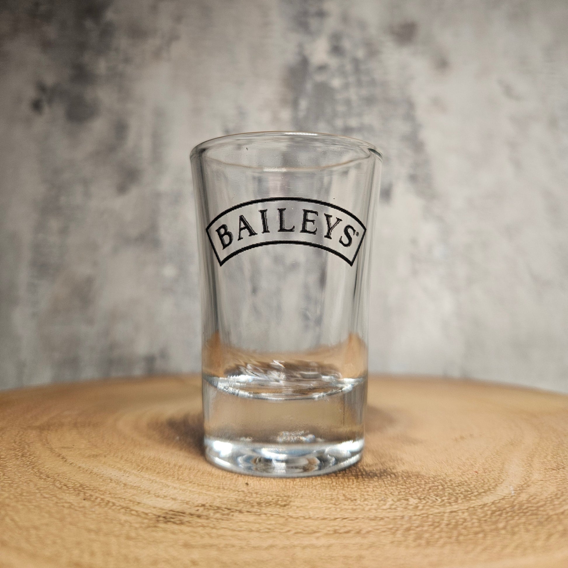Clear glass with 'Baileys' branding on a wooden surface and gray background