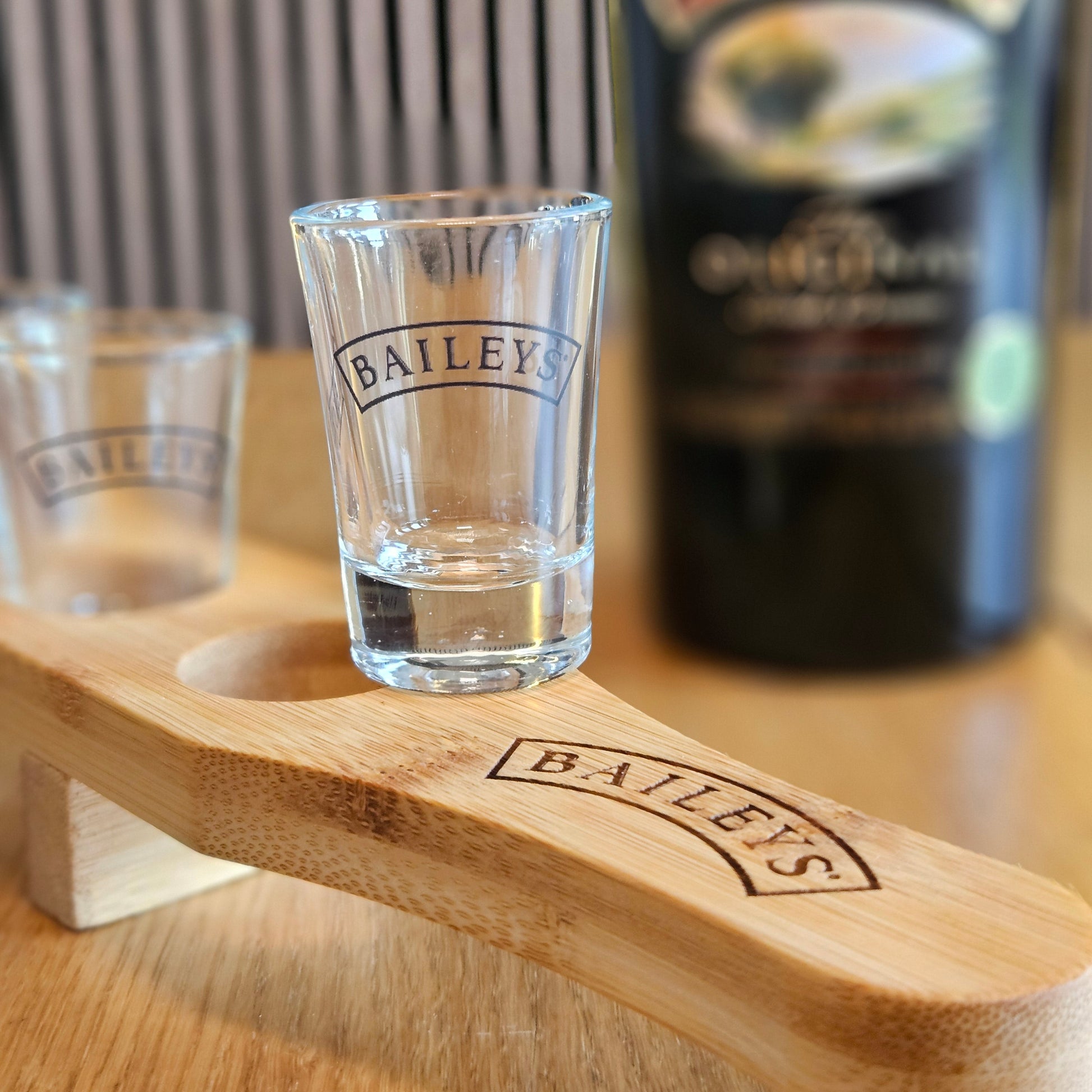 Baileys shot glasses on a wooden stand with a blurred bottle in the background.