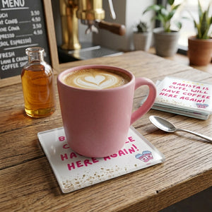 A square clear glass coaster with a white printed background featuring the phrase 'BARISTA IS CUTE, WILL HAVE COFFEE HERE AGAIN!' in pink lettering, five yellow stars at the top, coffee beans at the bottom, and two small pink-and-white takeaway coffee cups with hearts. A pink mug of coffee sits ontop of the coaster