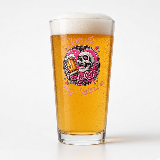 A pint glass filled with golden beer and topped with white foam, featuring a colorful graphic of a skull holding a beer mug surrounded by pink roses and the text 'Beer Is My Valentine'.