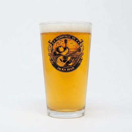 A clear pint glass filled with golden beer and topped with white foam, featuring a circular black graphic on the front that reads 'Nashville TN Jacks Beer' with a guitar and cowboy hat illustration, photographed on a white background.
