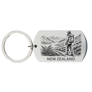 New Zealand backpacker keyring laser engraved stainless steel dog tag with female backpacker mountain peaks and native New Zealand wilderness scene on white background
