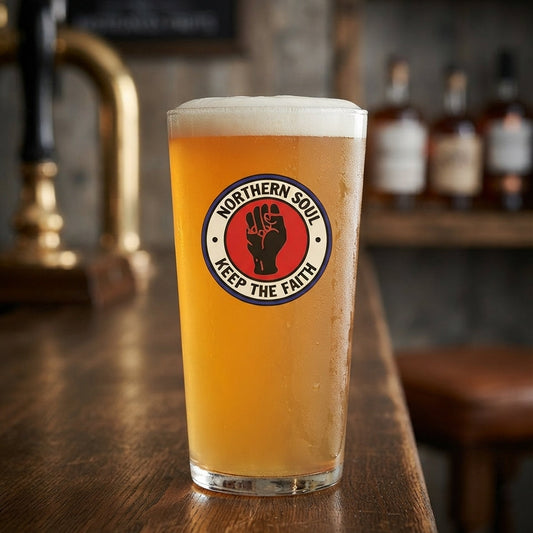 A pint of golden beer in a clear glass with a circular Northern Soul 'Keep The Faith' logo, set on a wooden bar counter with a blurred pub background.