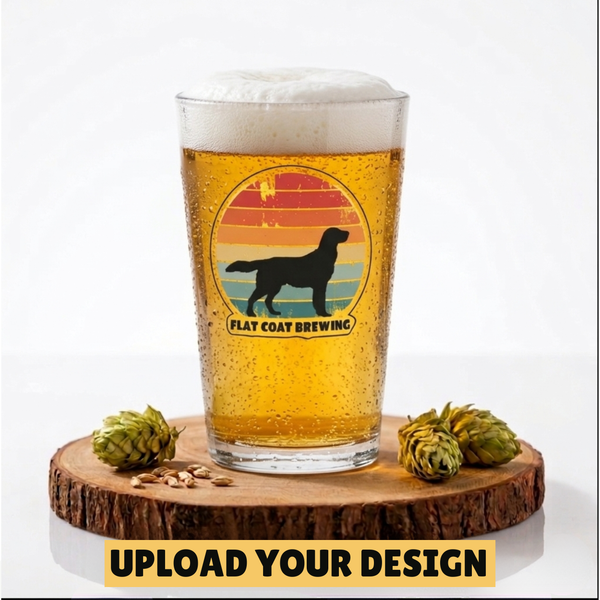 Pint glass with a beer design featuring a silhouette of a dog and 'Flat Coat Brewing' text, on a wooden coaster with hops and pine cones.