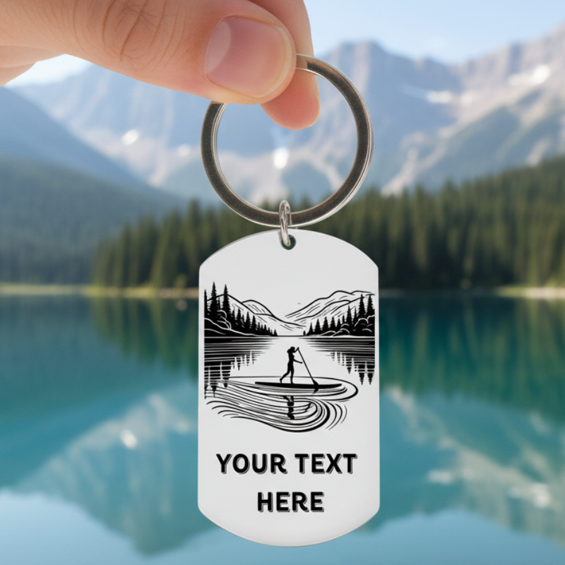Personalised laser engraved paddleboard keyring held against mountain lake with SUP silhouette and custom text, unique watersports gift