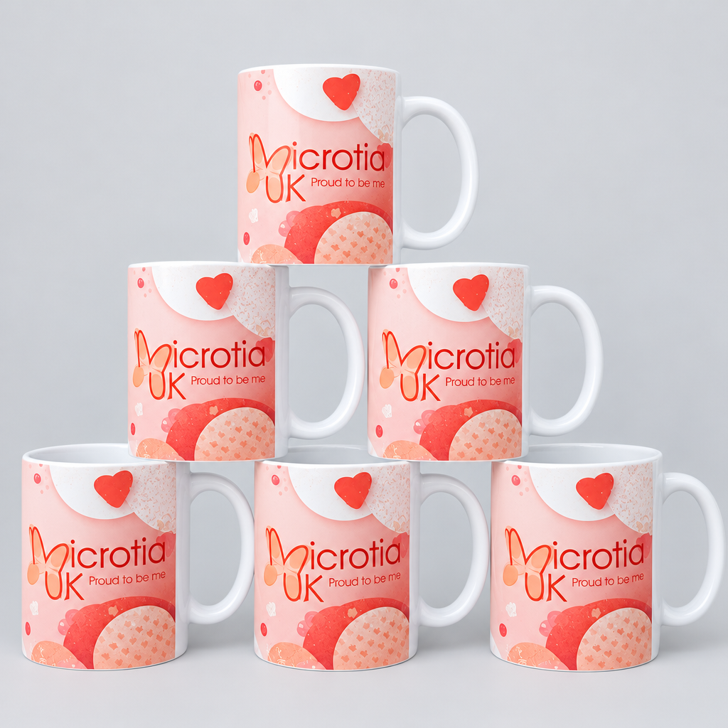 Six white ceramic mugs printed with a peach and orange strawberry-themed design and the text 'Microtia UK proud to be' are arranged in a pyramid on a wooden surface against a light stone-tile wall.