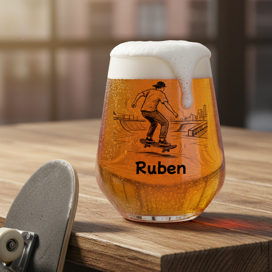 A stemless wine glass filled with amber beer and topped with white foam, printed with a skateboarder illustration and the name 'Ruben', sitting on a wooden table next to a skateboard.