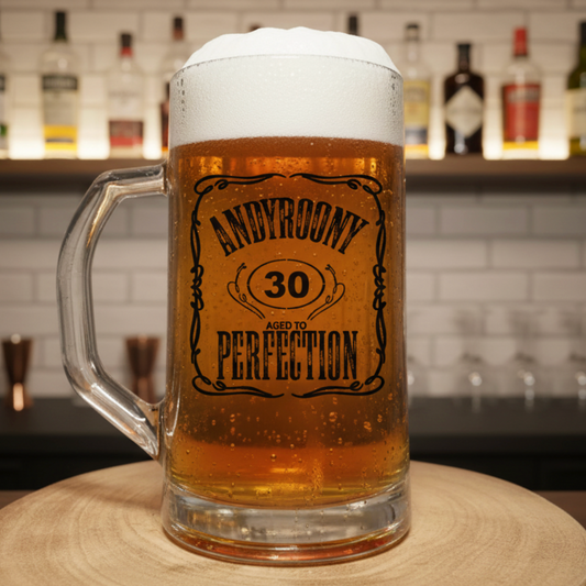 "Personalised 'Aged to Perfection' beer mug featuring custom name and milestone age in ornate label design, filled with beer and frothy head, set in front of bar background