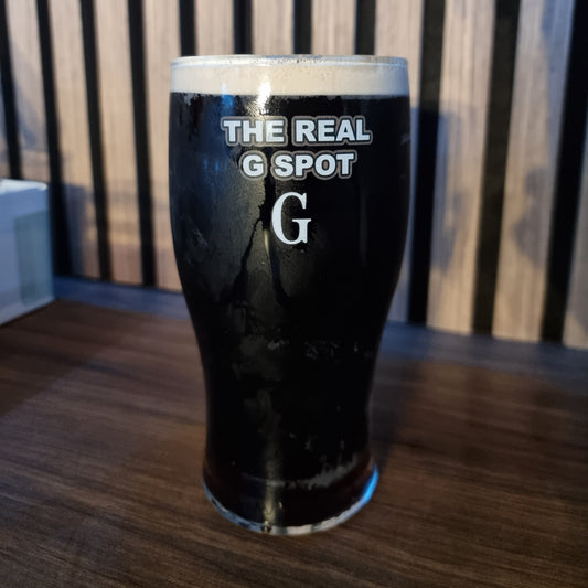 Real G Spot pint glass filled with dark Irish stout beer on a wooden bar