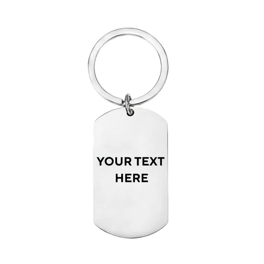 A silver metal dog tag keychain with a circular key ring, featuring the placeholder text 'YOUR TEXT HERE' printed in black on the front, set against a plain white background.