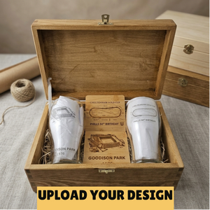 A wooden gift box with an open lid displays engraved glassware and a custom card in a styled setting. The set includes two white-wrapped glasses and a central card reading 'Cheltenham Gold Cup' and 'Phillies 50th Birthday,' with 'Goodison Park' engraved on the card.
