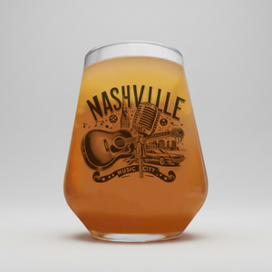 A stemless wine glass filled with an amber-colored beverage, featuring a black graphic print of a microphone, guitar, car, and the words 'NASHVILLE MUSIC CITY' on the front, set against a neutral gray background.