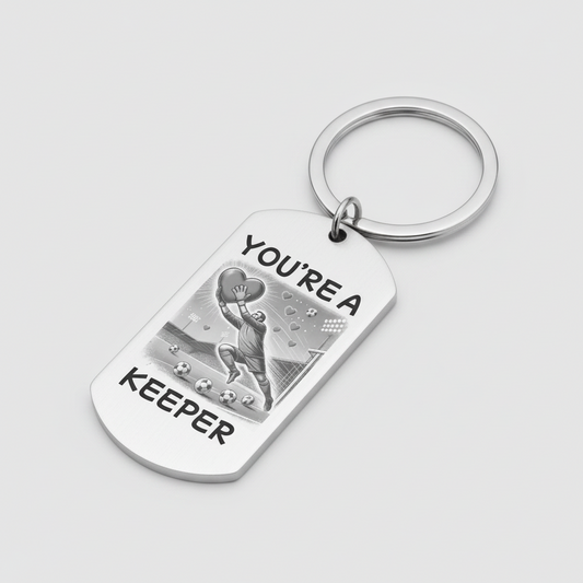 A silver metal dog tag keychain with a key ring, featuring a black and white illustration of a soccer player and the text 'YOU'RE A KEEPER' on a light gray background.